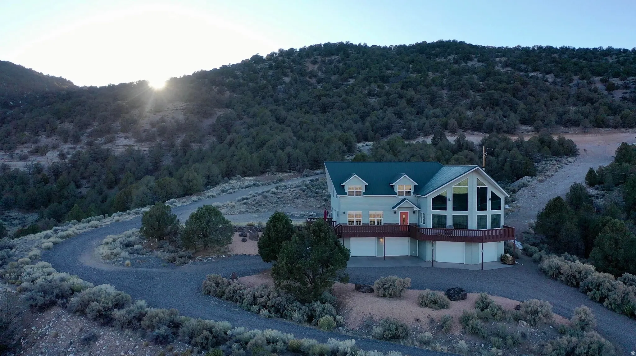Hillside residence featuring multiple garage bays, a wrap-around deck, and abundant natural landscaping