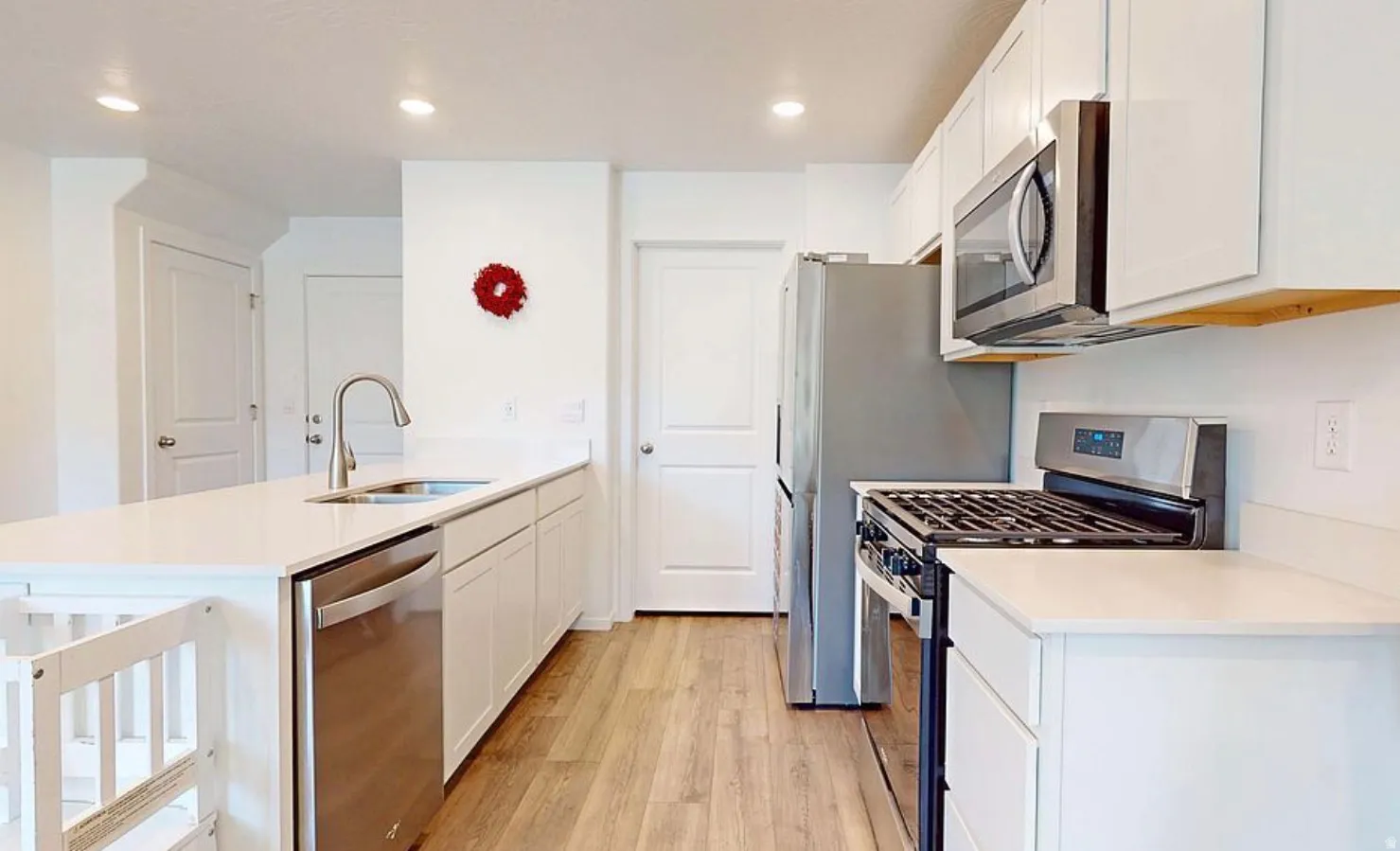 Modern kitchen featuring white cabinetry, light wood-finish flooring, stainless steel appliances, a gas range, and ample counter space with an integrated sink