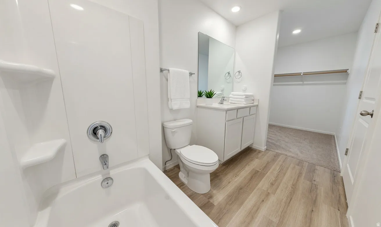Full bathroom featuring a white tub-shower combination with chrome fixtures, a single-sink vanity with white cabinetry, and wood-finish flooring