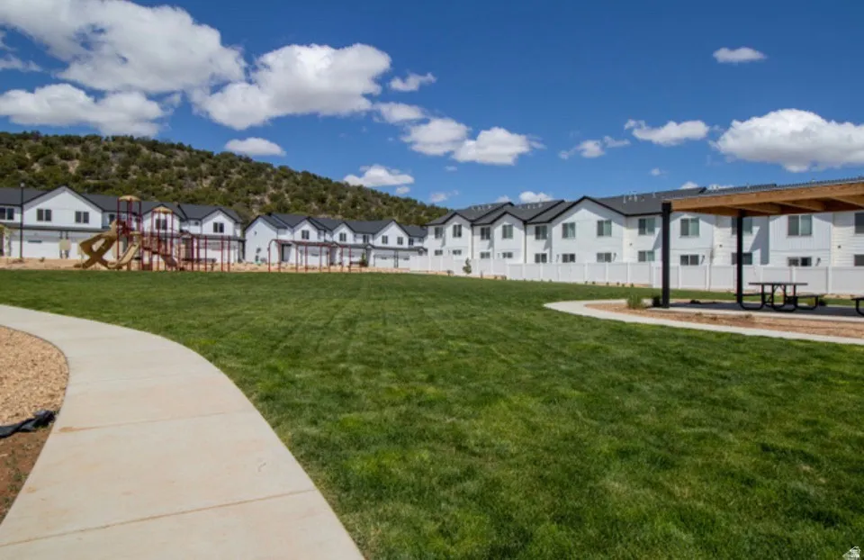 Expansive green space featuring a concrete pathway, a play structure, and a covered picnic area