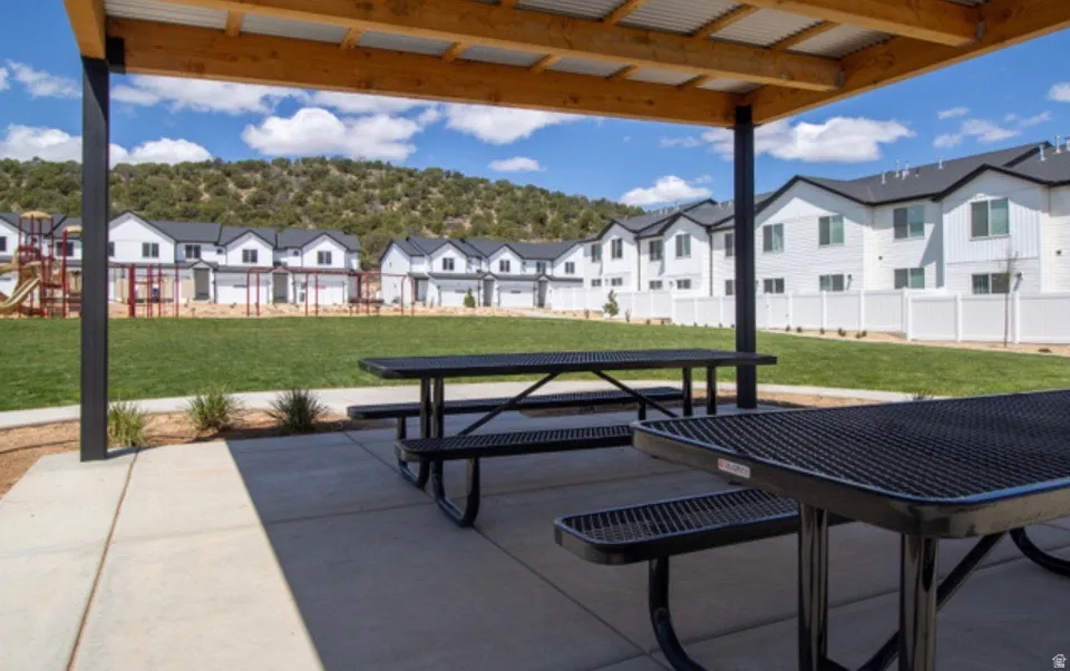 Community common area featuring a covered picnic pavilion with multiple picnic tables, a manicured lawn, and a playground