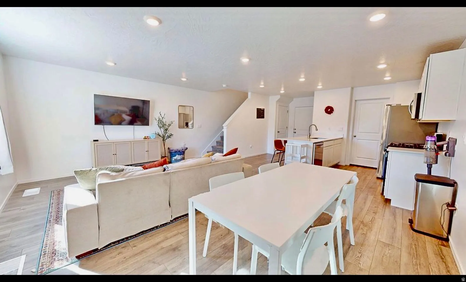 Open-concept living area featuring recessed lighting, wood-finish flooring, a kitchen island with seating, white cabinetry, and stainless steel appliances
