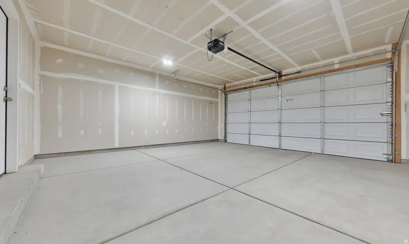 Spacious two-car garage featuring a concrete floor, an overhead garage door opener, and interior lighting