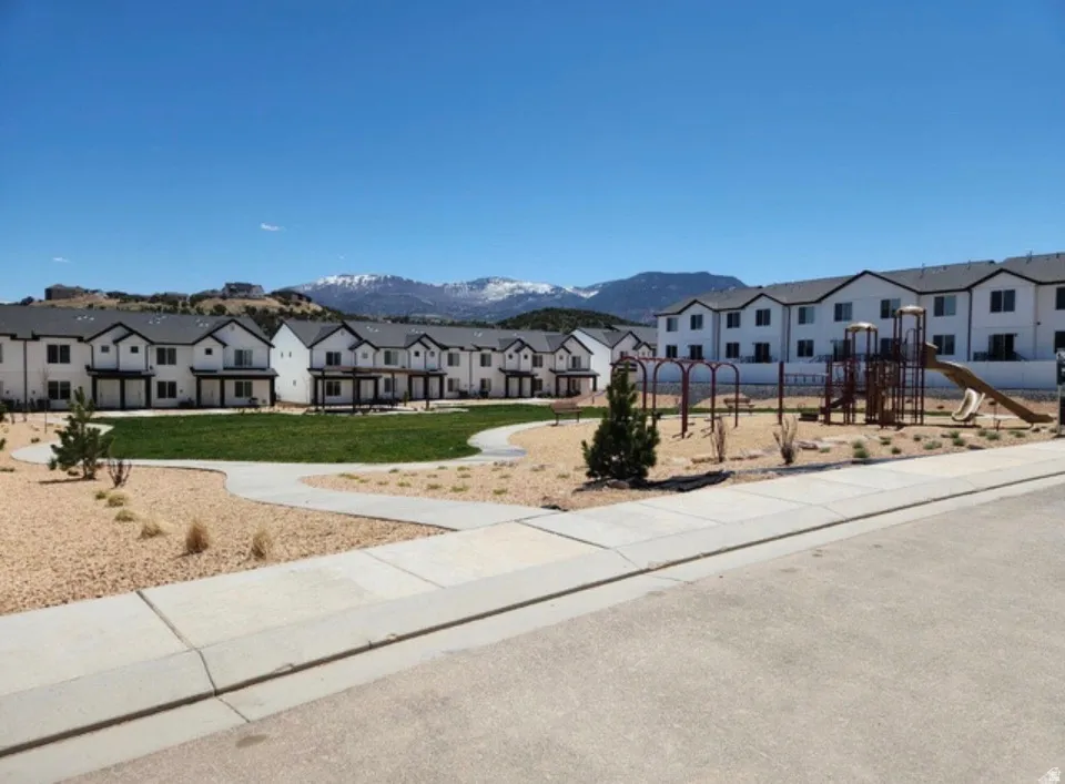Community green space featuring a manicured lawn, paved walkways, and a dedicated playground area