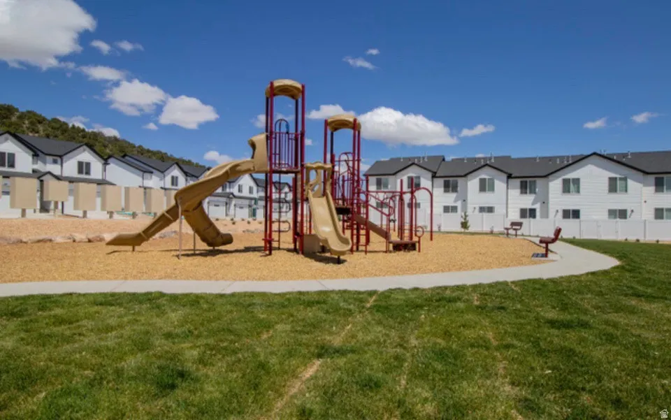 Community playground area with a multi-level play structure, wood chip base, and a curved concrete path