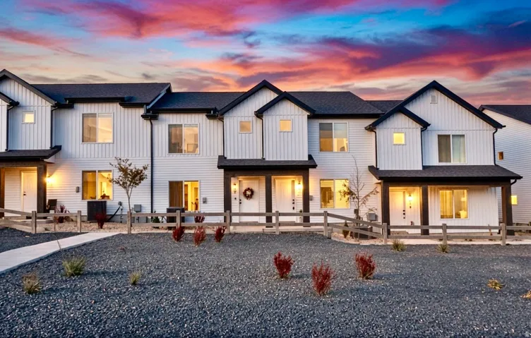 Modern multi-story townhomes with white vertical and horizontal siding, black trim, and dark roofing