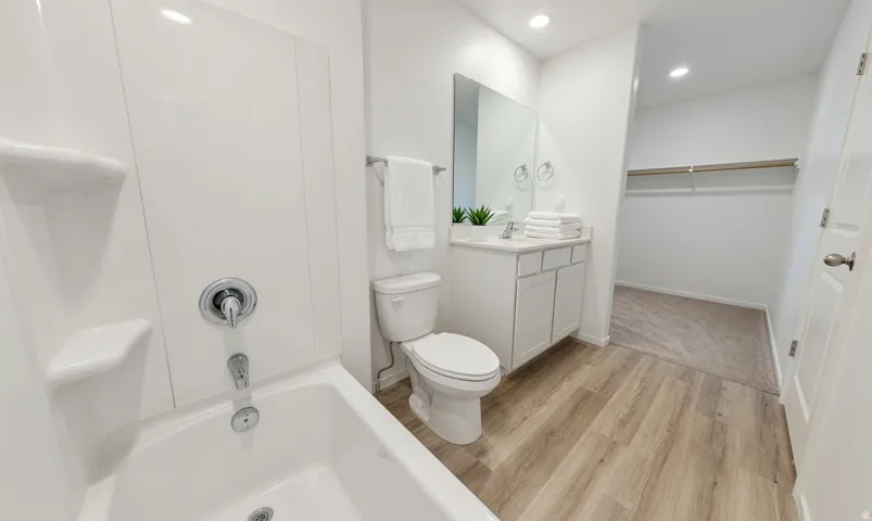 Full bathroom featuring a white tub-shower combination with chrome fixtures, a single-sink vanity with white cabinetry, and wood-finish flooring