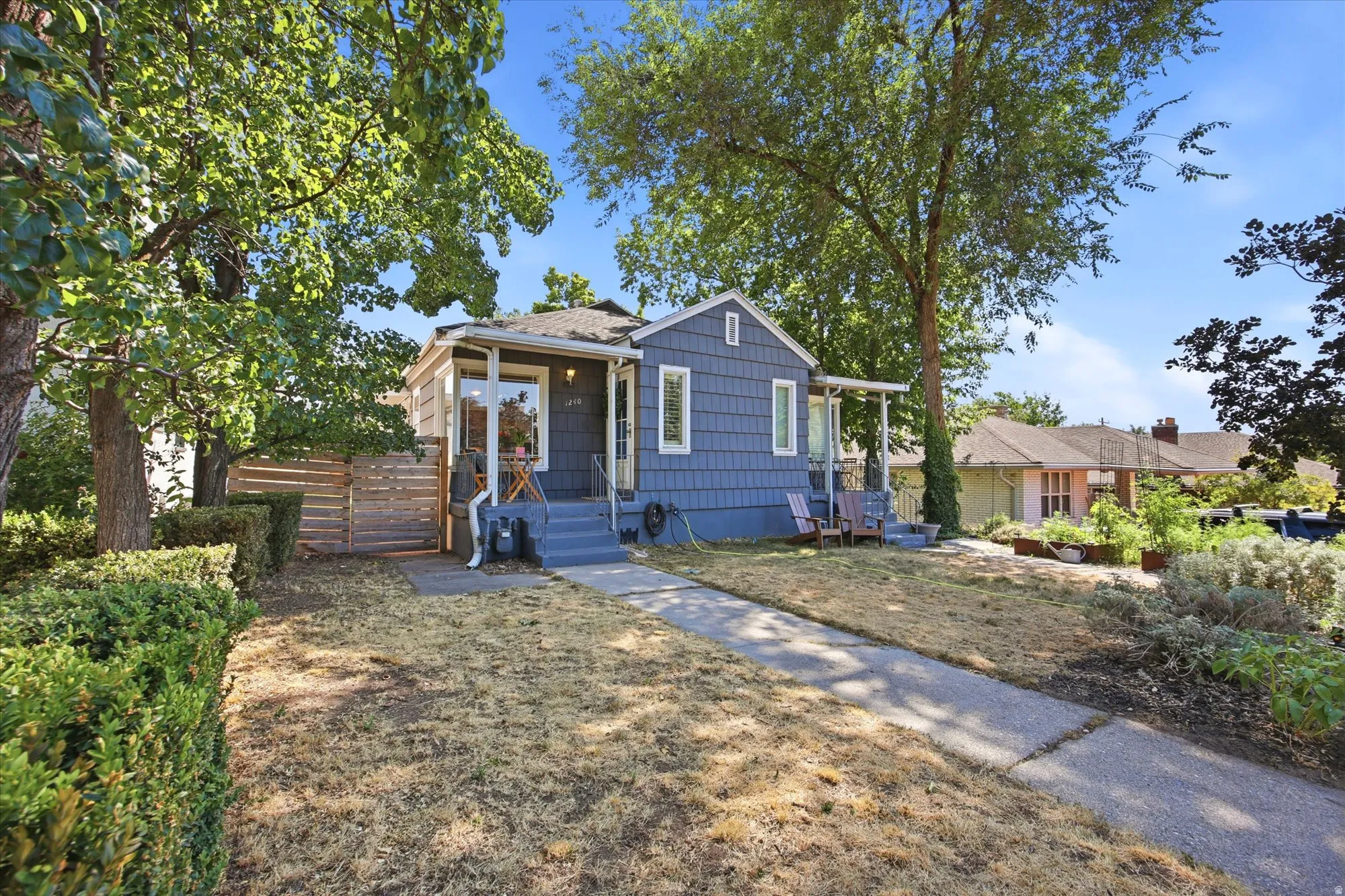 Charming bungalow exterior featuring blue shingle siding, a covered front porch, and mature trees providing natural shade