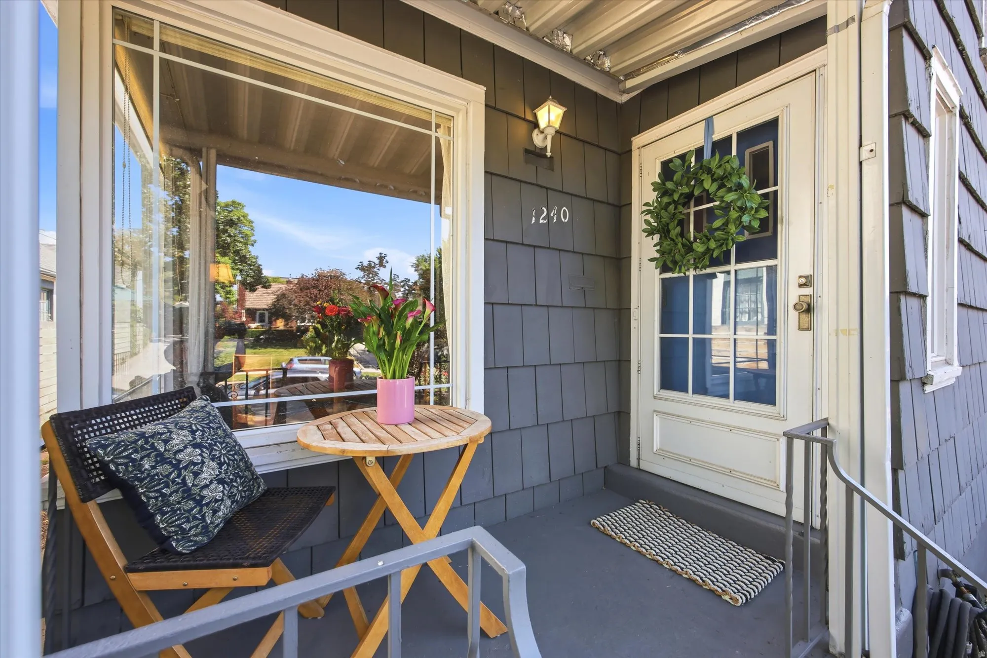 Covered front porch featuring gray shingle siding, a multi-pane front door with white trim, and a wall-mounted light fixture