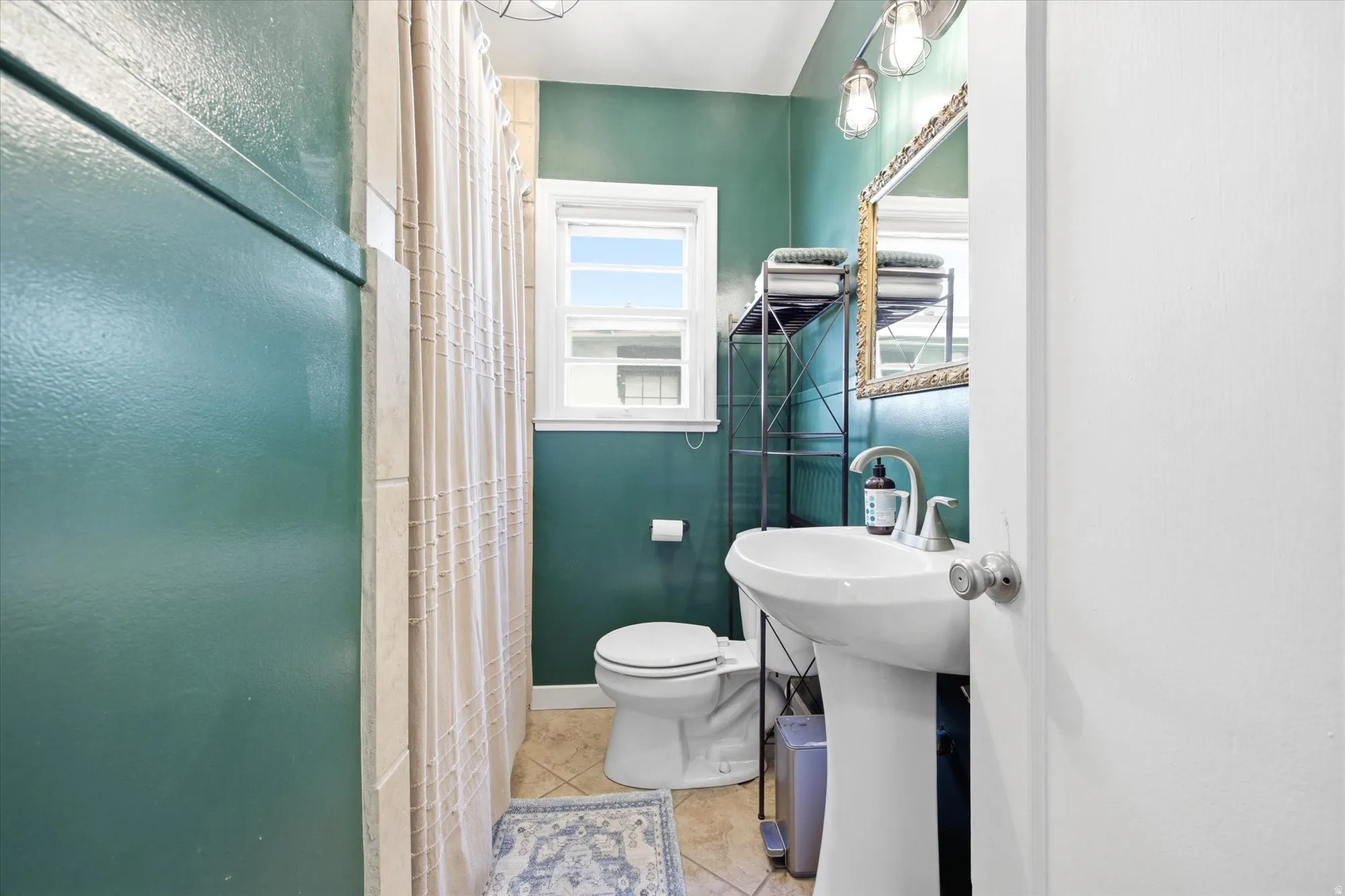 Pedestal sink with chrome faucet, complemented by a decorative mirror and sconce lighting