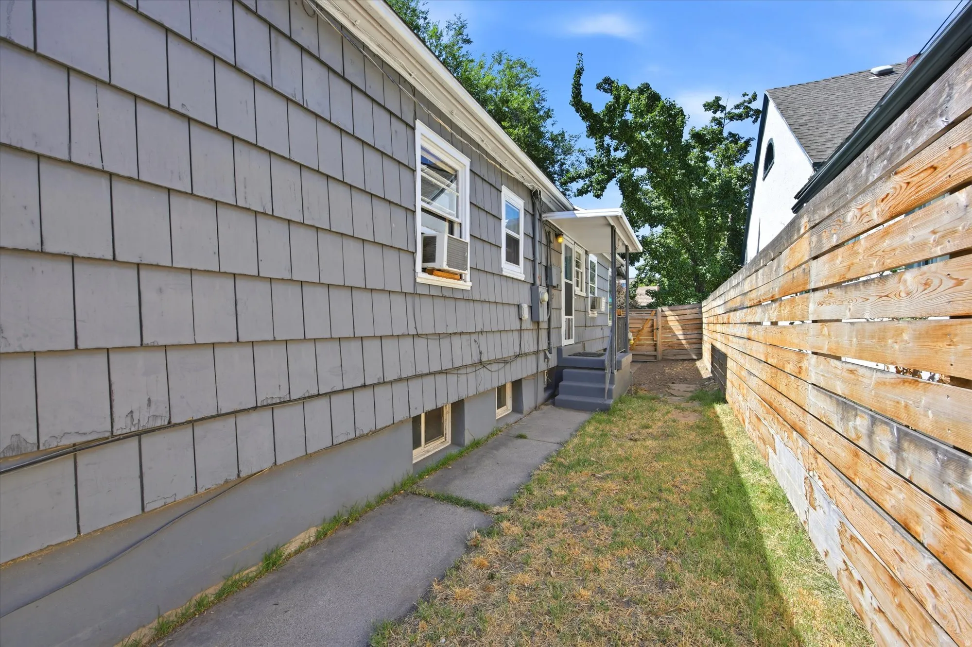 Exterior siding featuring gray shingles, a privacy fence crafted from horizontal wood slats, and a concrete pathway