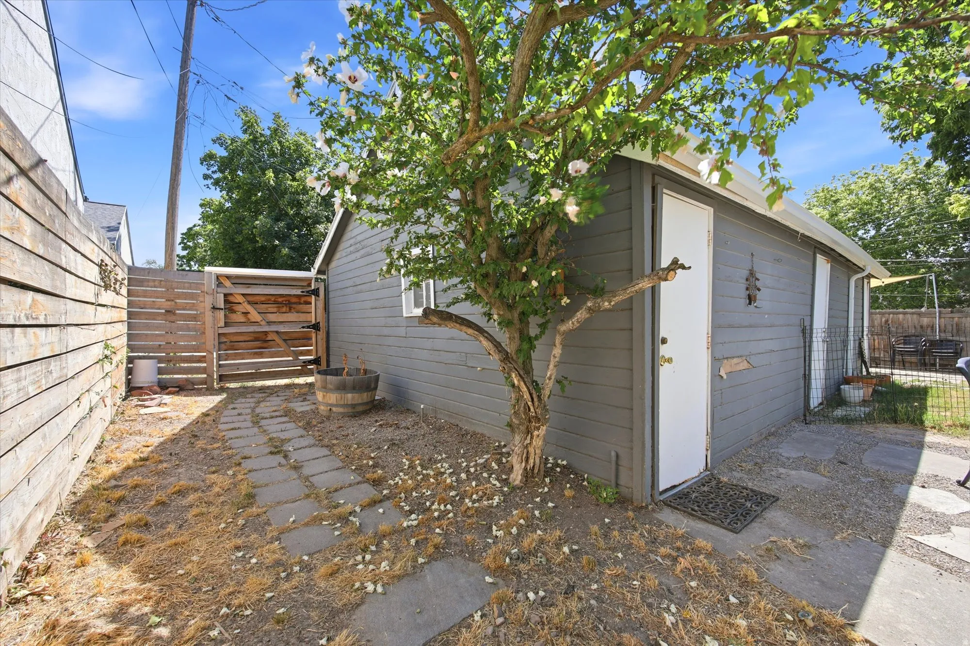 Side yard featuring a painted wood-sided outbuilding with white entry door, a privacy fence with a wood gate, and a concrete paver pathway