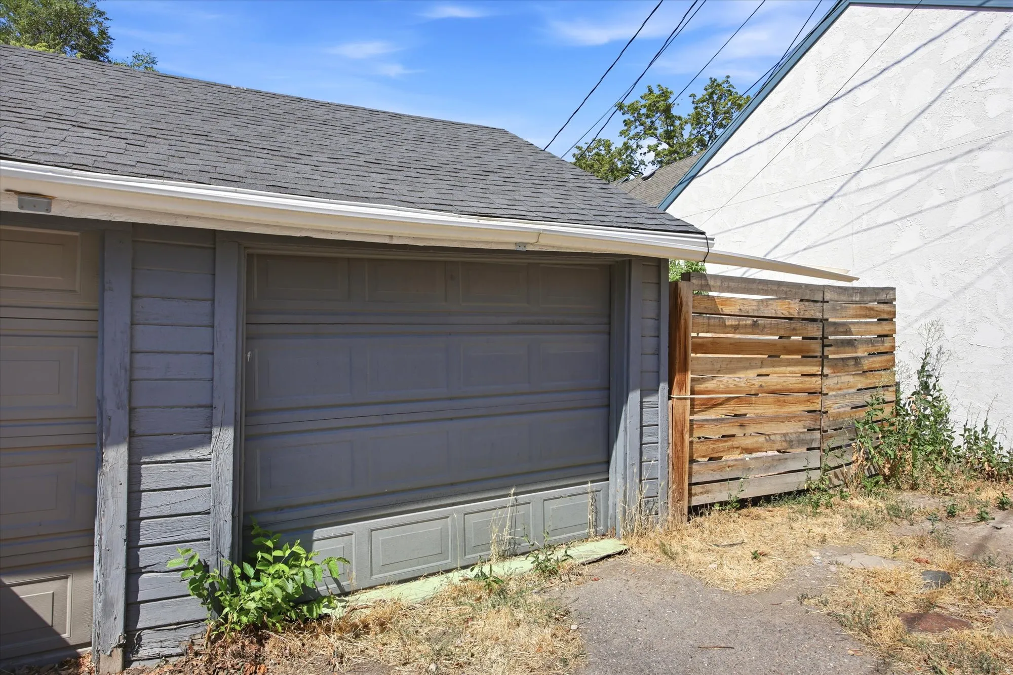 Garage structure featuring a gray panel door, horizontal siding, and a shingled roof with white gutters
