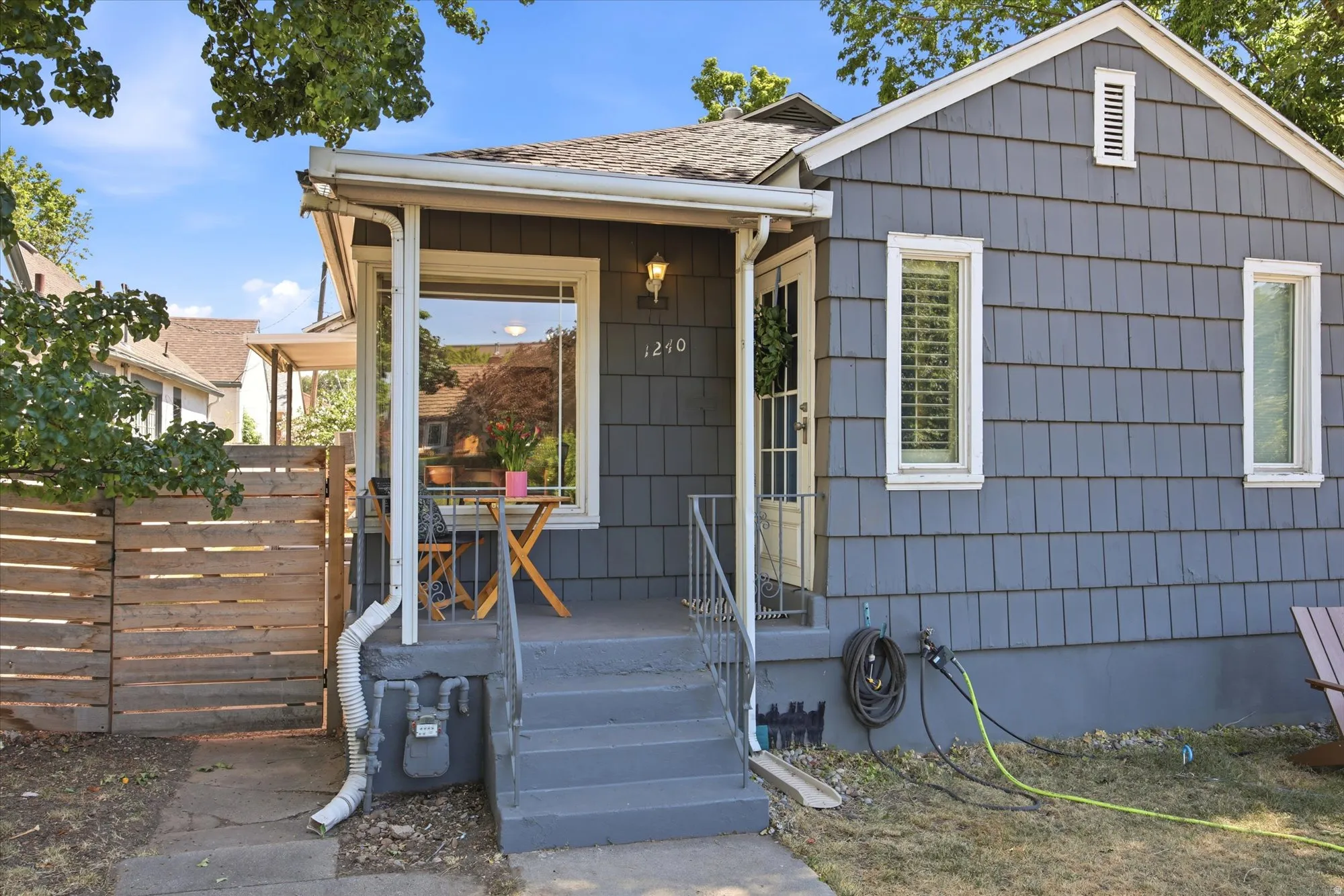 Charming bungalow exterior featuring gray shingle siding, a covered front porch, and a wooden privacy fence