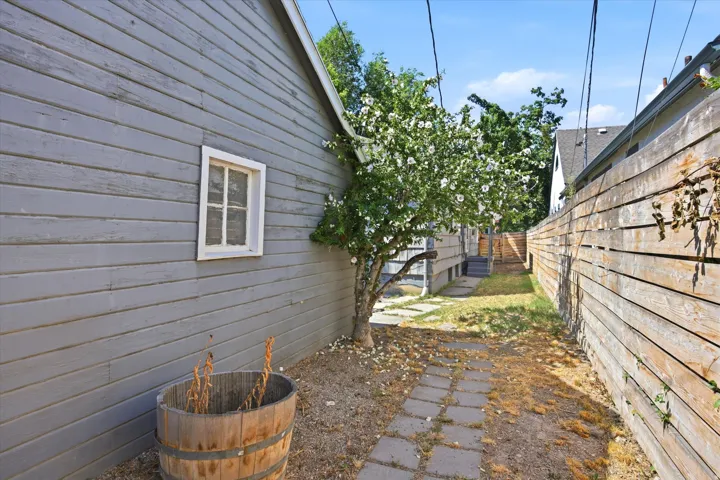 Sideyard featuring a stone paver pathway, mature flowering tree, and horizontal plank fencing