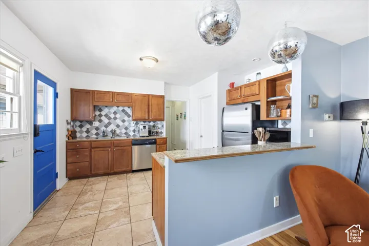 Kitchen featuring wood cabinetry, stainless steel dishwasher, tile backsplash with a geometric pattern, and tiled flooring