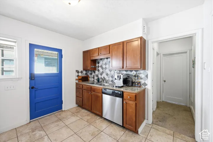 Kitchen area featuring wood cabinetry, stainless steel dishwasher, tile flooring, and a patterned tile backsplash