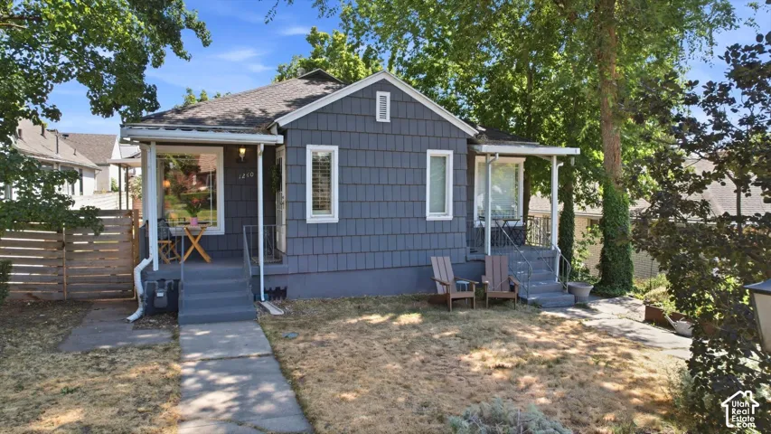 Shingle siding exterior with a covered front porch, concrete pathway, and mature trees