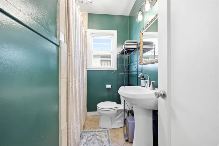 Pedestal sink with chrome faucet, complemented by a decorative mirror and sconce lighting
