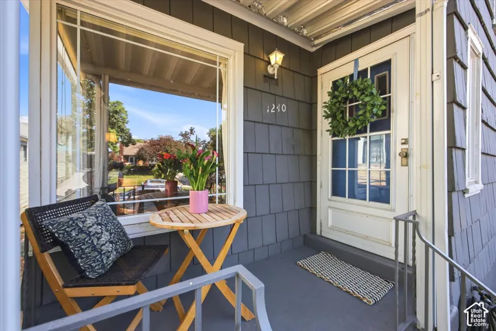 Covered front porch featuring gray shingle siding, a multi-pane front door with white trim, and a wall-mounted light fixture