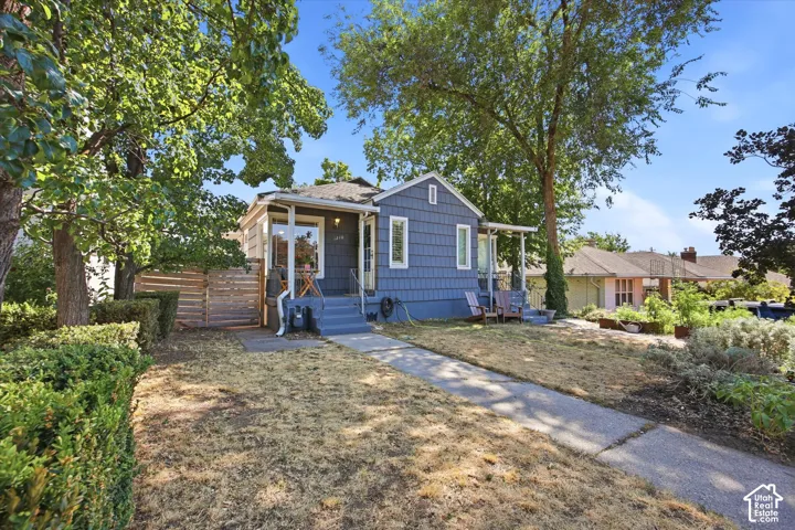 Charming bungalow exterior featuring blue shingle siding, a covered front porch, and mature trees providing natural shade