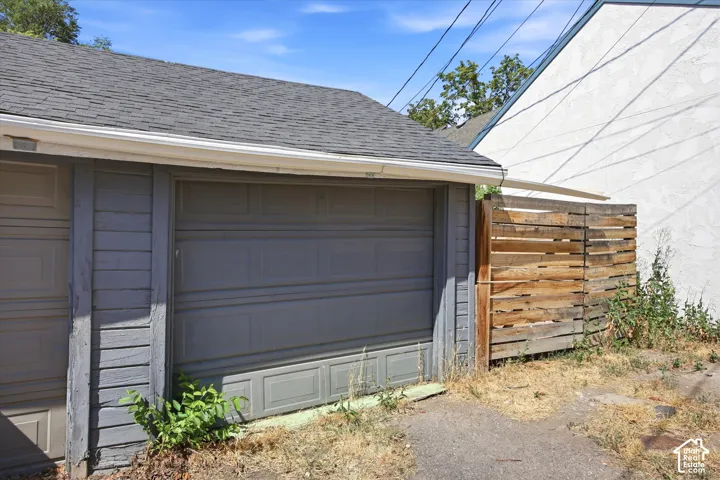 Garage structure featuring a gray panel door, horizontal siding, and a shingled roof with white gutters