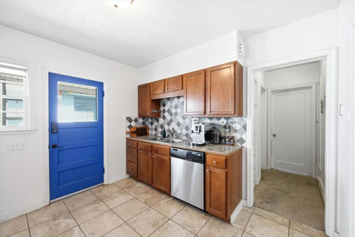 Kitchen area featuring wood cabinetry, stainless steel dishwasher, tile flooring, and a patterned tile backsplash