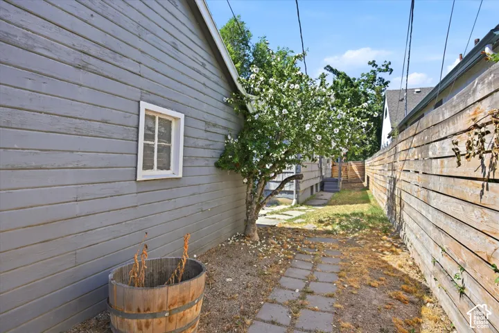 Sideyard featuring a stone paver pathway, mature flowering tree, and horizontal plank fencing