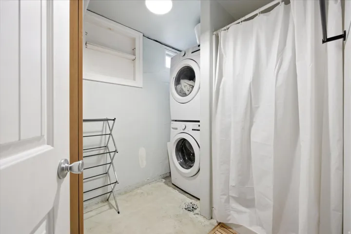 Compact laundry area with stacked washer and dryer, adjacent to a shower enclosure with a white curtain