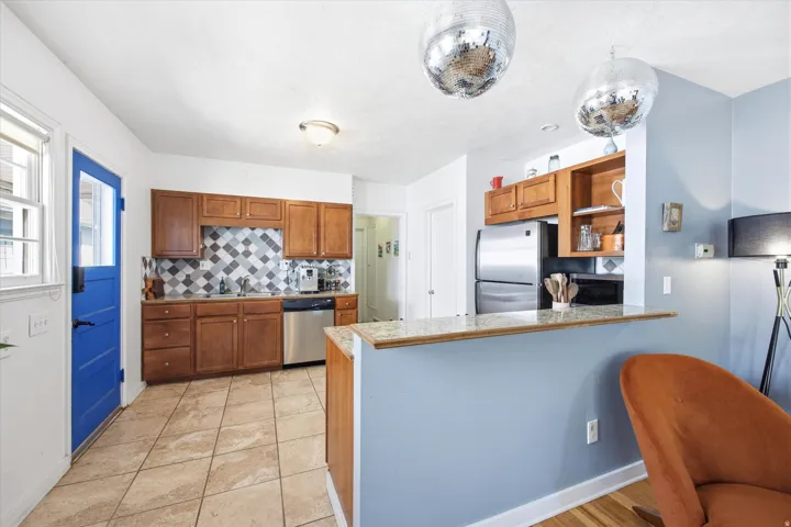 Kitchen featuring wood cabinetry, stainless steel dishwasher, tile backsplash with a geometric pattern, and tiled flooring