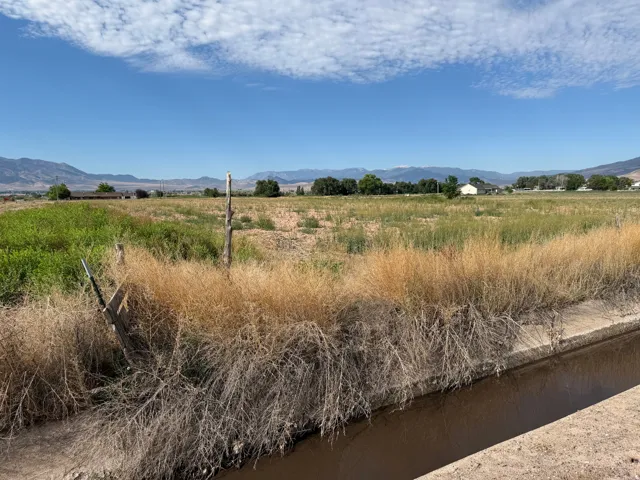 Expansive open land with a concrete-lined water channel, distant mountain scenery, and a clear blue sky