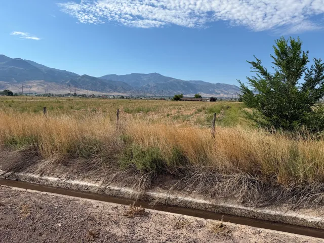 Expansive land parcel featuring natural grasses, a concrete irrigation ditch, and distant mountain ranges