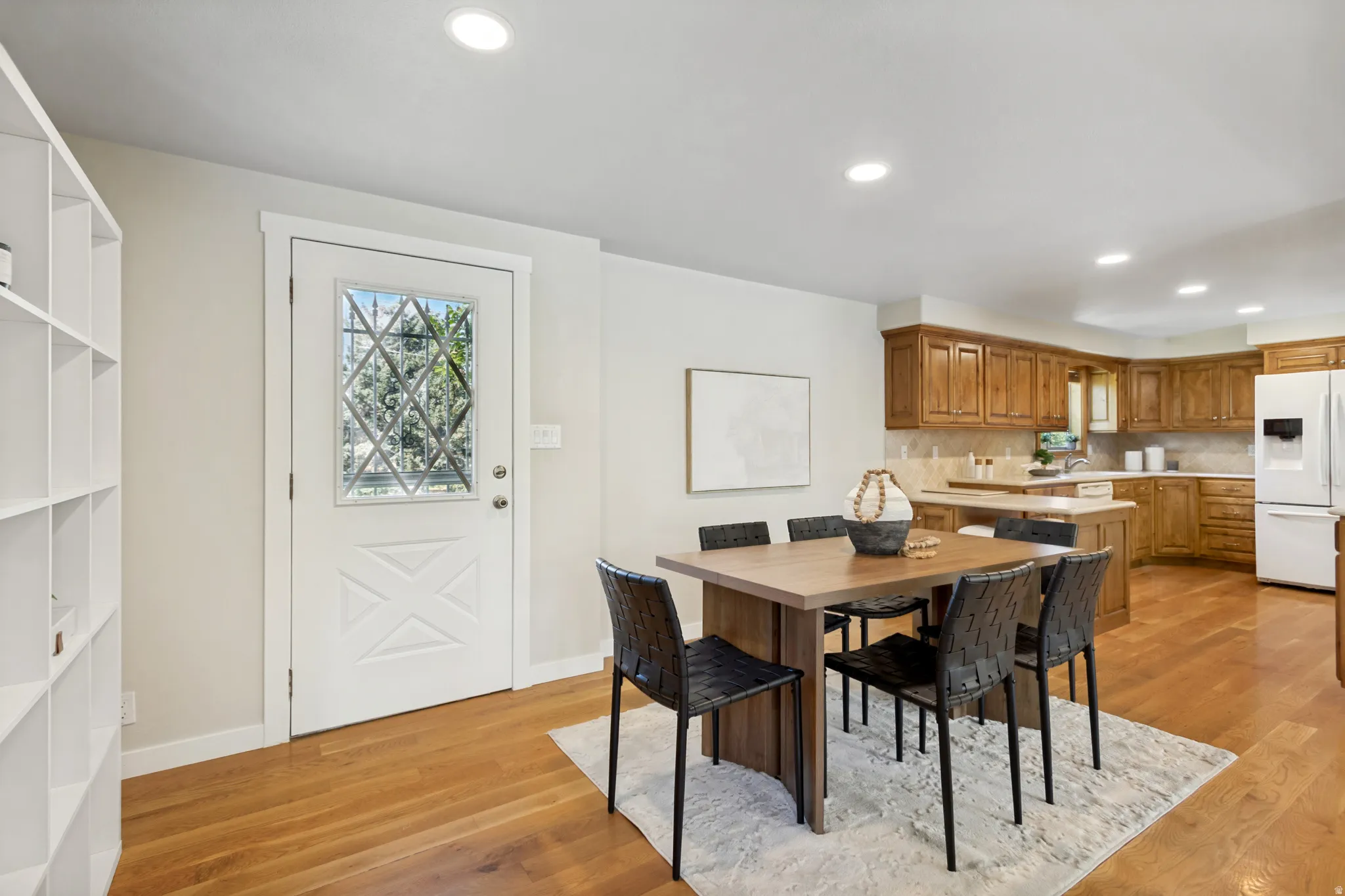 Open-concept living space featuring wood-finish flooring, recessed lighting, and a white entry door with decorative glass