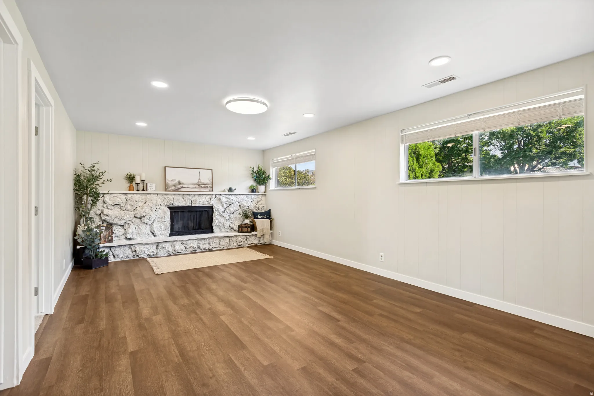 Spacious interior featuring wood-finish flooring, a stone fireplace, recessed lighting, and multiple windows