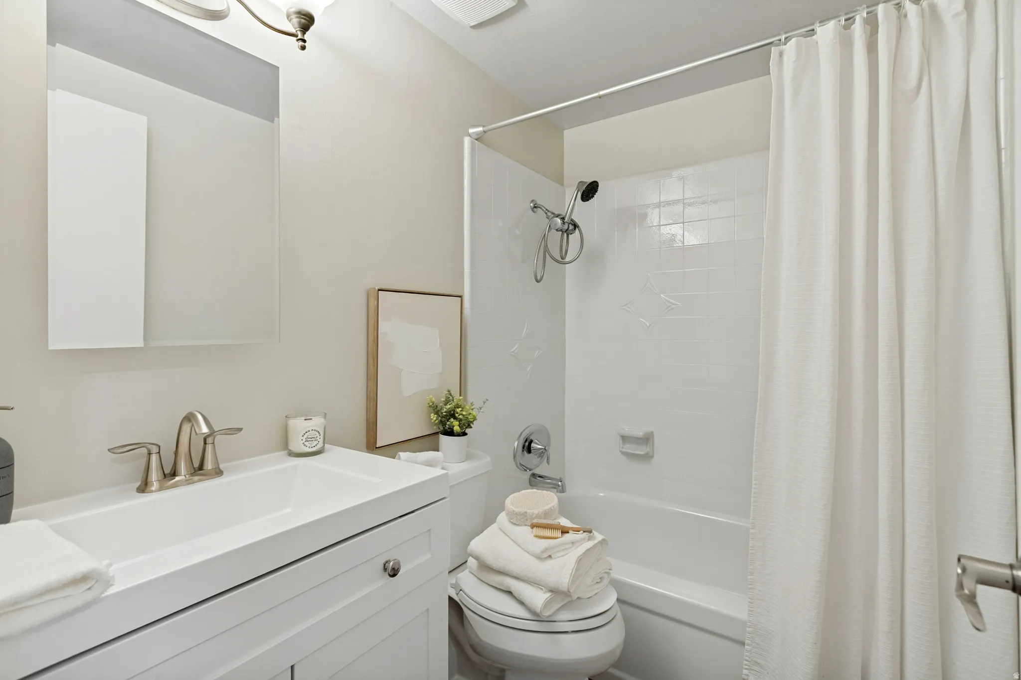 Main Bathroom featuring a white vanity with integrated sink, brushed nickel faucet, wall-mounted mirror, and a shower-over-tub combination with white subway tile surround