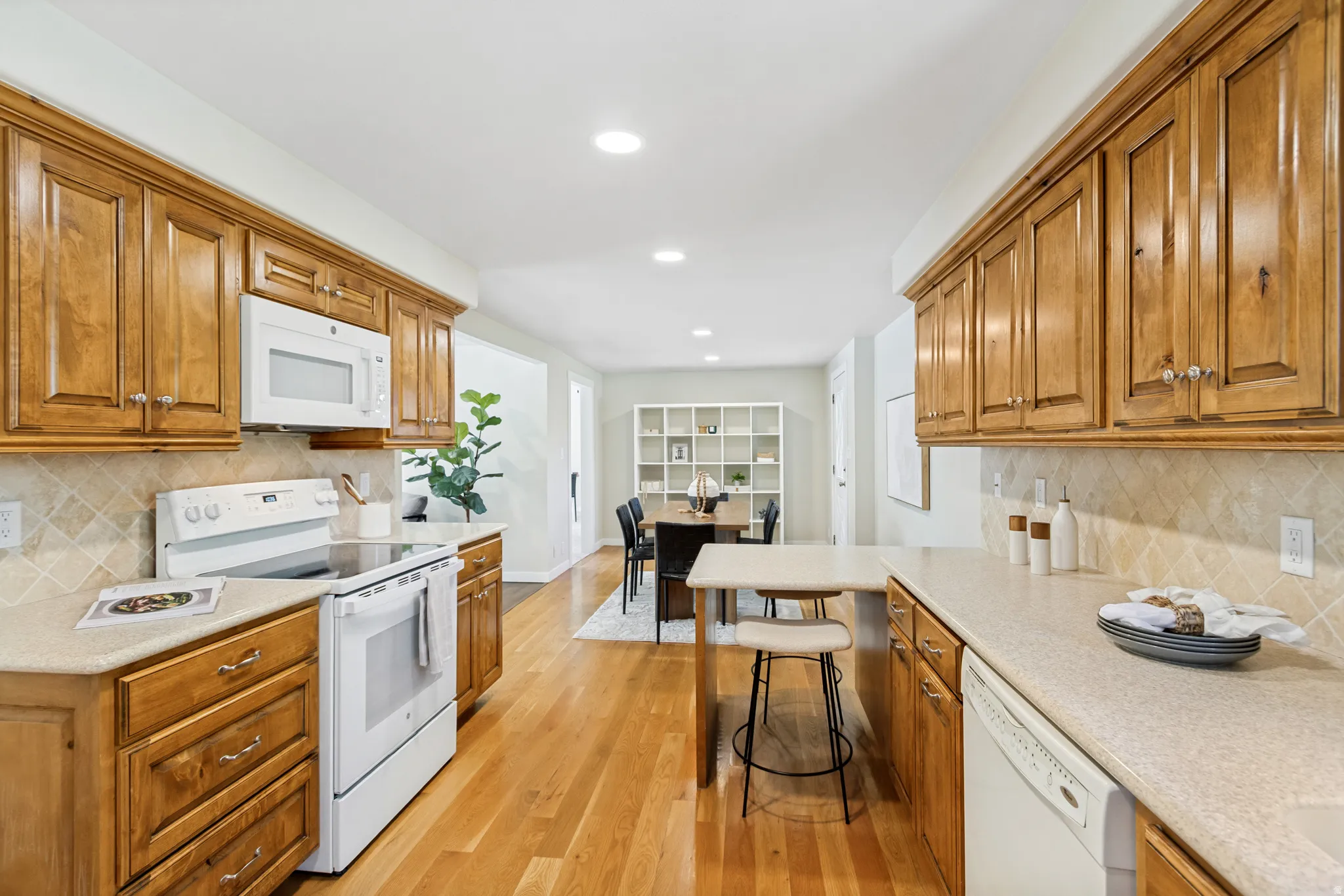 Kitchen featuring extensive wood cabinetry, light-toned countertops, white appliances, and a tiled backsplash