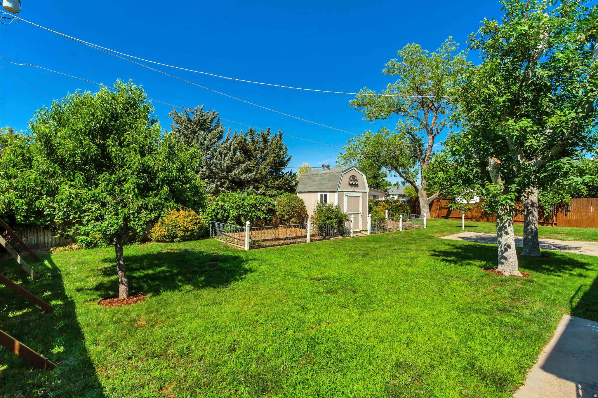 Spacious backyard featuring a storage shed with an arched dormer, mature trees, a manicured lawn, and perimeter fencing