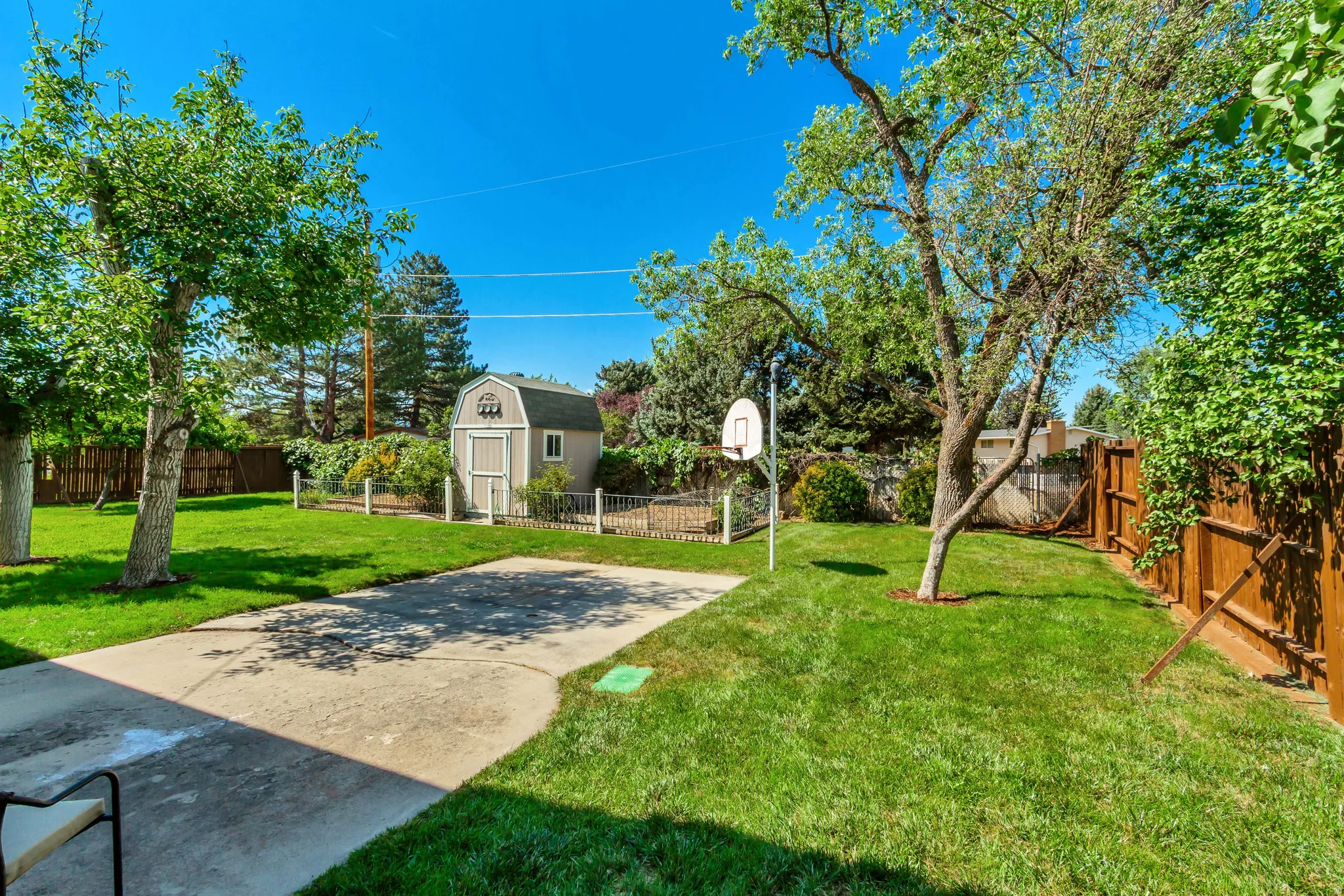Expansive backyard featuring a concrete patio, a detached shed with a gambrel roof, mature trees, and wooden privacy fencing