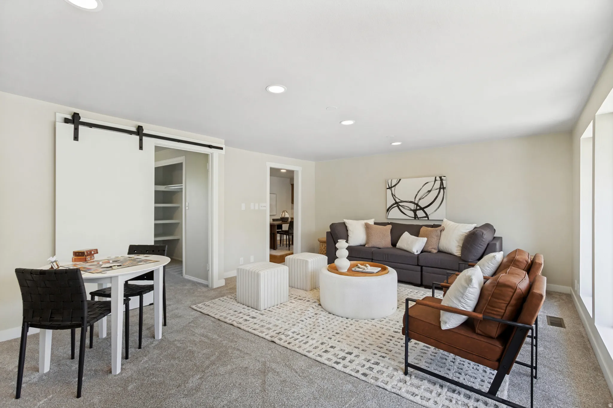 Versatile living area featuring soft gray carpeting, recessed lighting, and ample natural light from large windows
