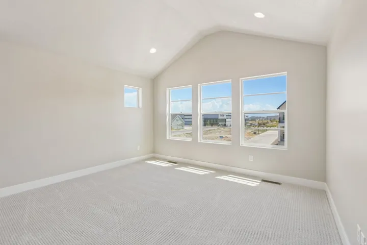 Spacious room featuring a vaulted ceiling with recessed lighting, multiple windows providing natural illumination, light-colored walls, and textured carpeting