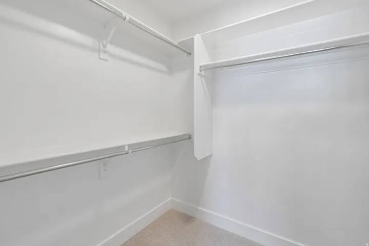 Walk-in closet featuring white painted walls and trim, light-toned carpet flooring, and multiple built-in shelving and hanging rods