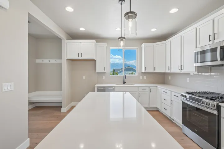 Spacious kitchen featuring an expansive island, white cabinetry, integrated stainless steel appliances, pendant lighting, and wood-finish flooring