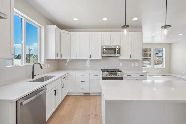 Modern kitchen featuring white shaker cabinetry, stainless steel appliances, a gas range, light-toned wood-finish flooring, and pendant lighting
