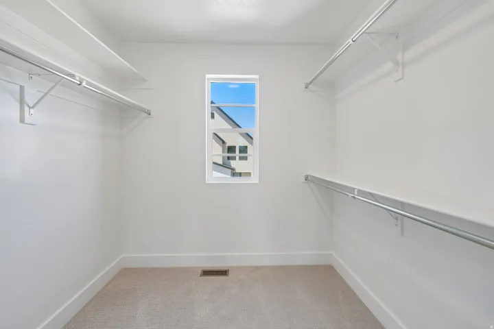 Walk-in closet featuring light-colored carpeting, white walls, and a window providing natural light