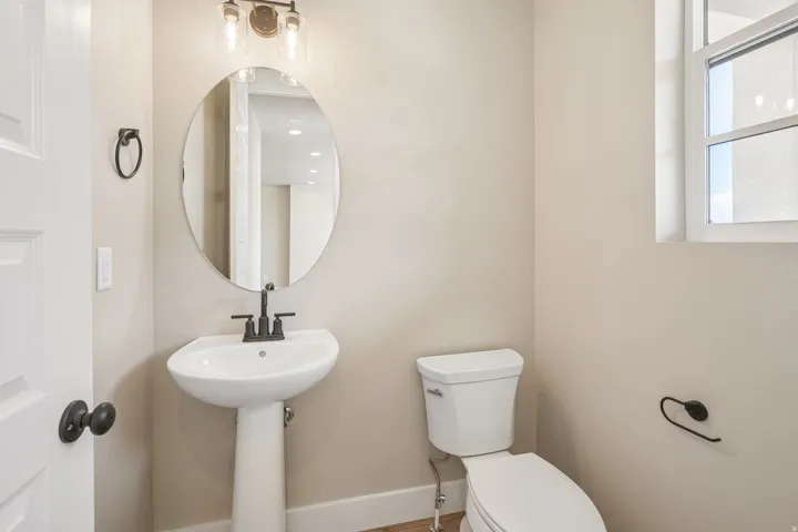Pedestal sink with a matte black faucet, oval mirror, and a three-light vanity fixture