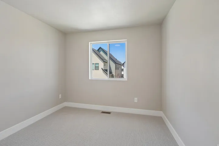 Neutral-toned room featuring a single window, light gray carpeting, crisp white baseboards, and a contemporary electrical outlet