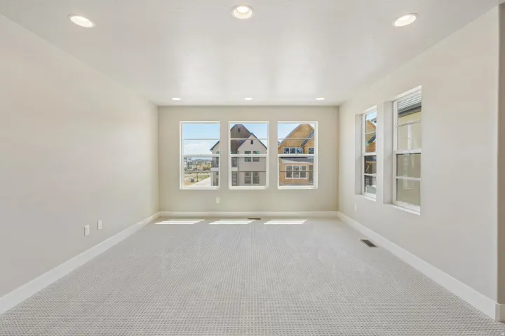 Spacious room featuring multiple windows, recessed lighting, neutral wall paint, white trim, and light-toned patterned carpet