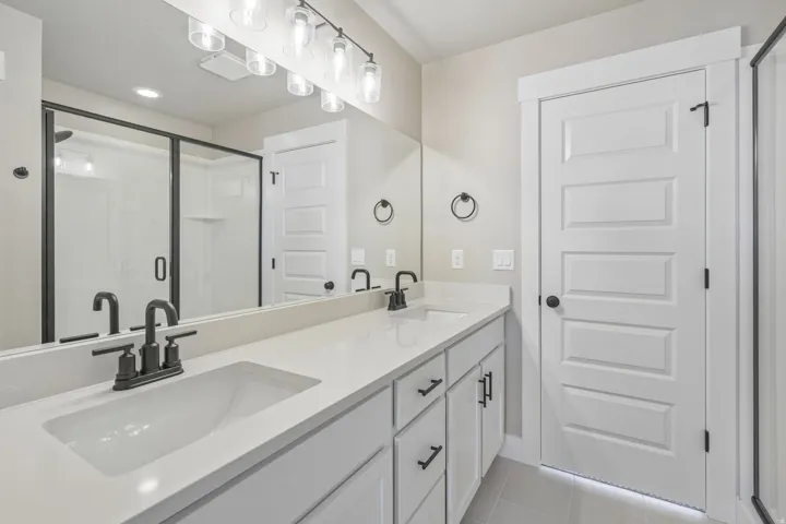Dual vanity with quartz countertops, integrated sinks, matte black hardware, and a framed glass shower enclosure