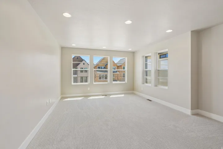 Spacious room featuring light-colored carpeting, multiple windows, recessed lighting, and neutral wall paint