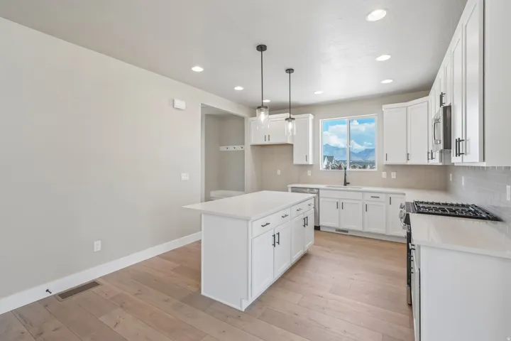 Contemporary kitchen featuring an island with a light-toned countertop, white cabinetry with dark hardware, a gas range, and wood-finish flooring